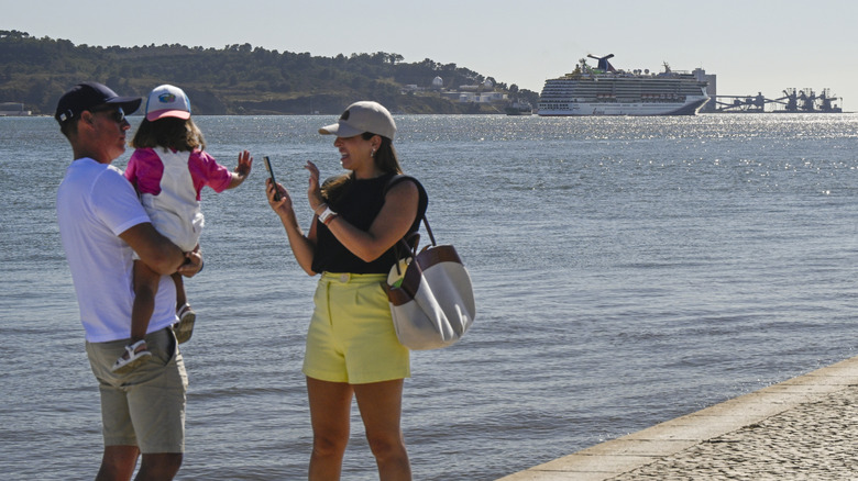 Cruise vacationers taking a selfie on the beach in Portugal with a Carnival Cruise Line ship in the background