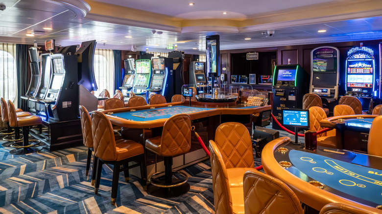 Upscale casino room onboard an Oceania cruise ship, with quilted cognac leather charis surrounding craps tables and slot machines