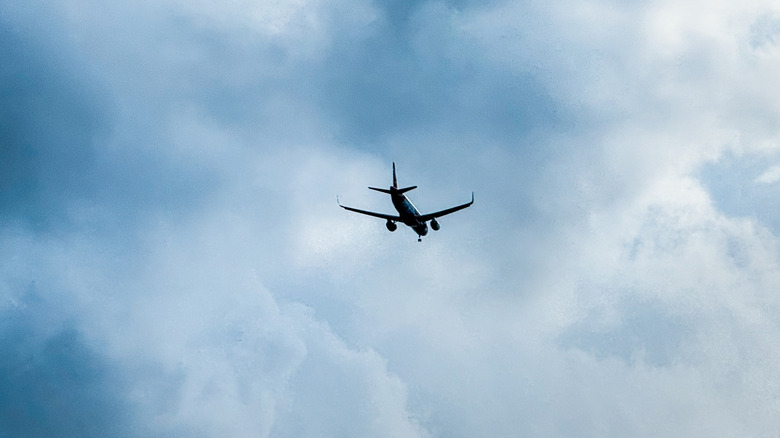 Silhouette of a plane flying high into dark, stormy clouds