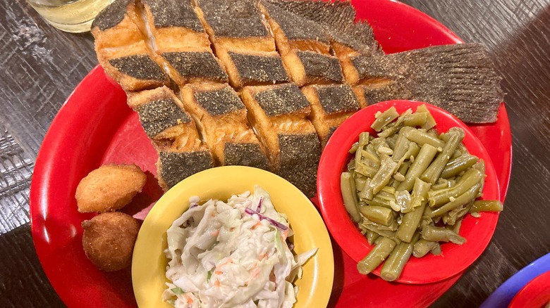 A loaded red dinner plate at Darrell's Seafood Restaurant in Manteo, North Carolina, featuring fried fish, coleslaw, green beans, and fried hush puppies