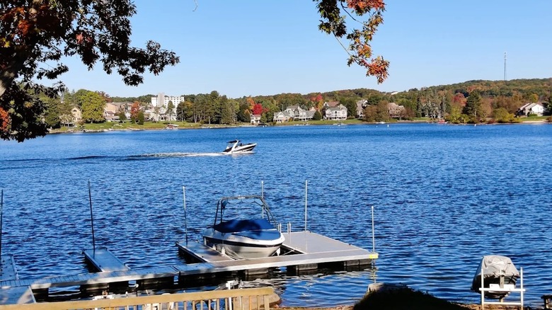 Small boat parked at a dock with a speed boat gliding by in the distance along the blue waters of Deep Creek Lake in Maryland