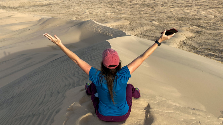 Person sitting on dunes with arms raised