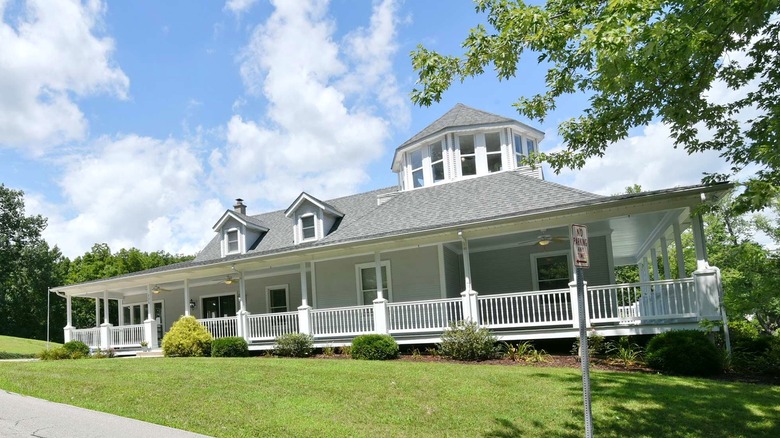 A large B&B house with a wraparound porch with white trim, a manicured lawn, and blue skies