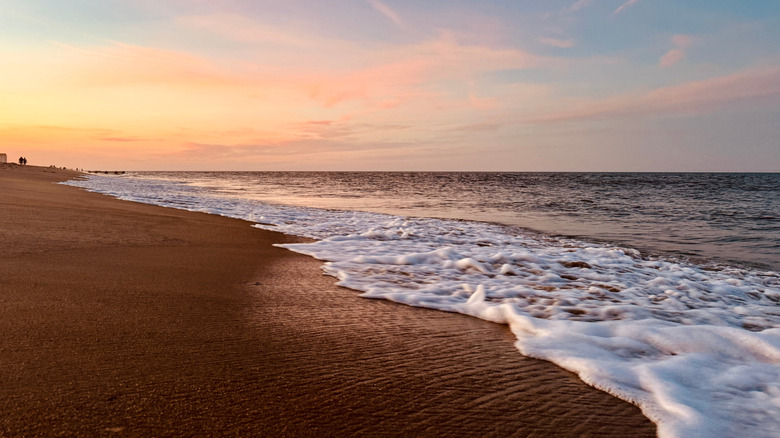 the sky turns orange and pink with the sunset as waves lap the shore of Rehoboth Beach, Delaware