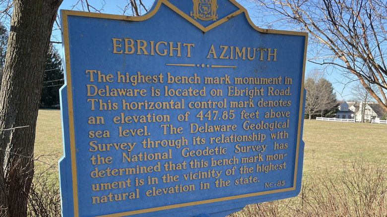 A blue heritage sign identifies Ebright Azimuth and explains its significance in front of a sunny field