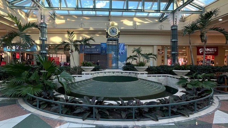 Dead fountain surrounded by plants and a clock tower with a skylight inside Concord Mall Delaware