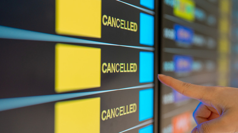 A sign at the airport lists multiple cancelled flights
