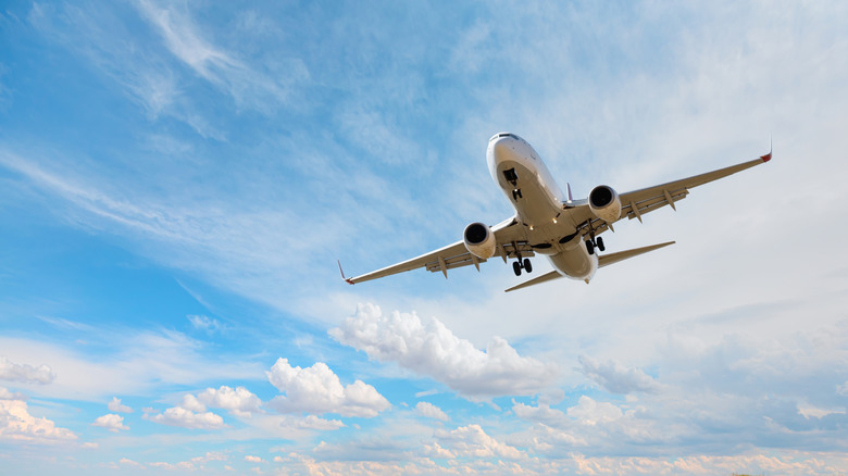 An airplane flying against a blue sky with scattered white clouds