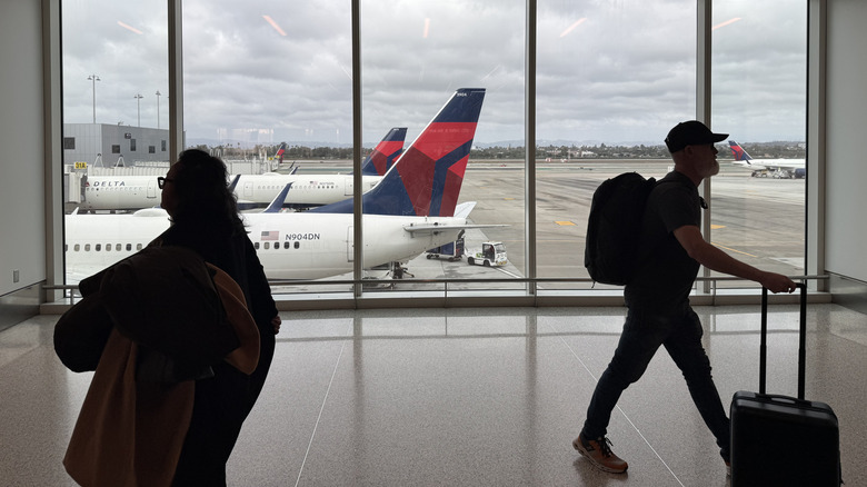 Passengers walking in airport terminal with Delta planes outside
