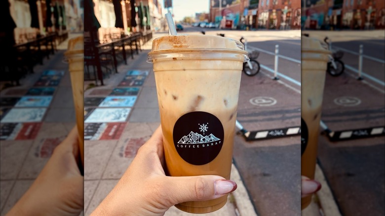 A hand holds up an iced coffee