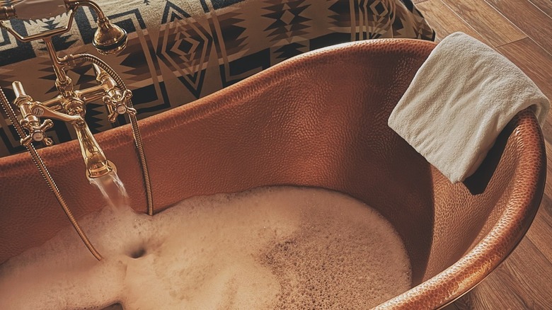 A hand-hammered brass clawfoot bathtub with a bubble bath in one of the suites