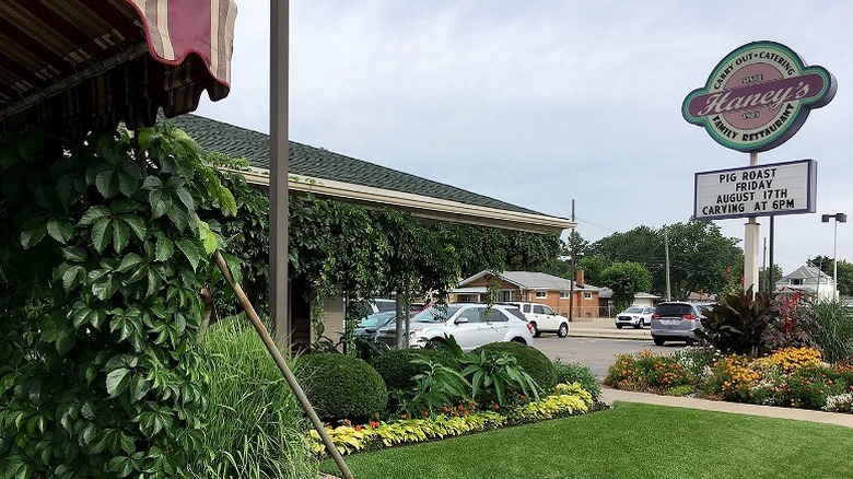 A gardened entry to Haney's Family Restaurant with cars parked and a tall sign.
