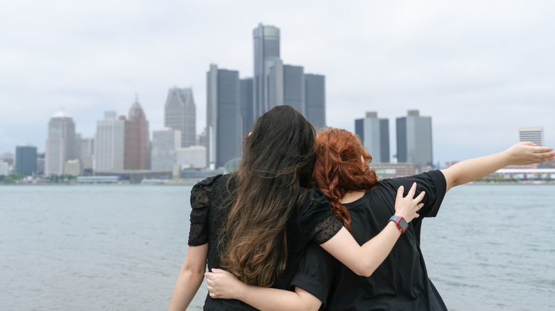 Two young women look across the water the skyline of Detroit, Michigan