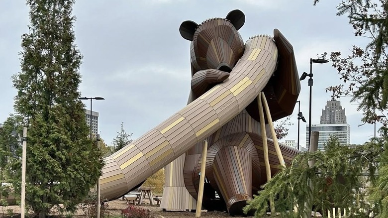 A view of the playgrond, showing a wooden bear sculpture holding a slide