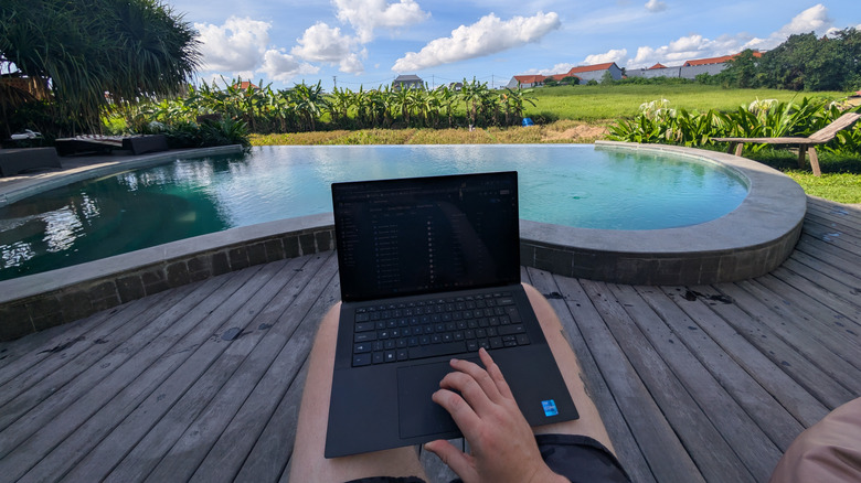 Worker typing on laptop near a Bali swimming pool with rice paddies