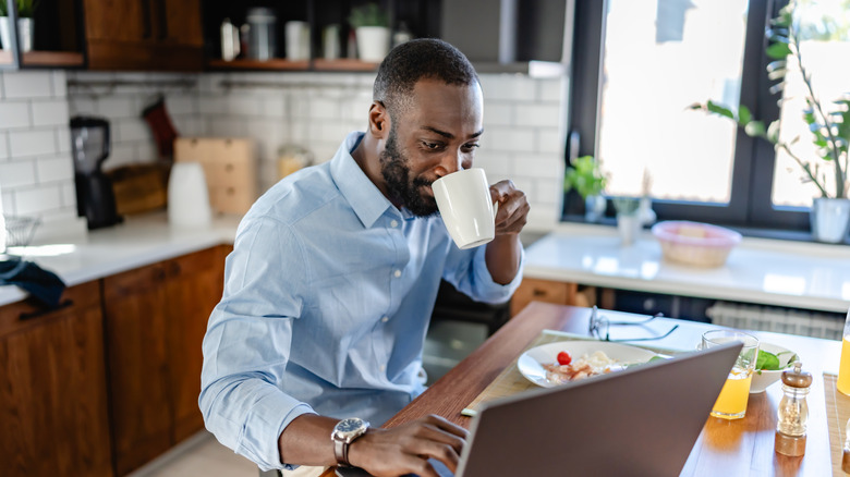 man working from his kitchen with a cup of coffee