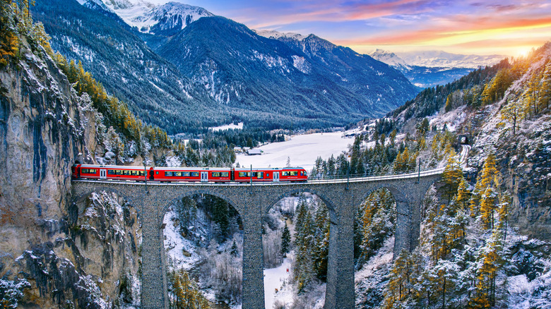 A red train crossed an historic bridge over an aqueduct in the Swiss Alps