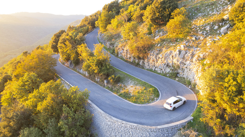 Drone view of a car driving on a picturesque but scary hairpin turn in the Italian lower Alps with fall foliage