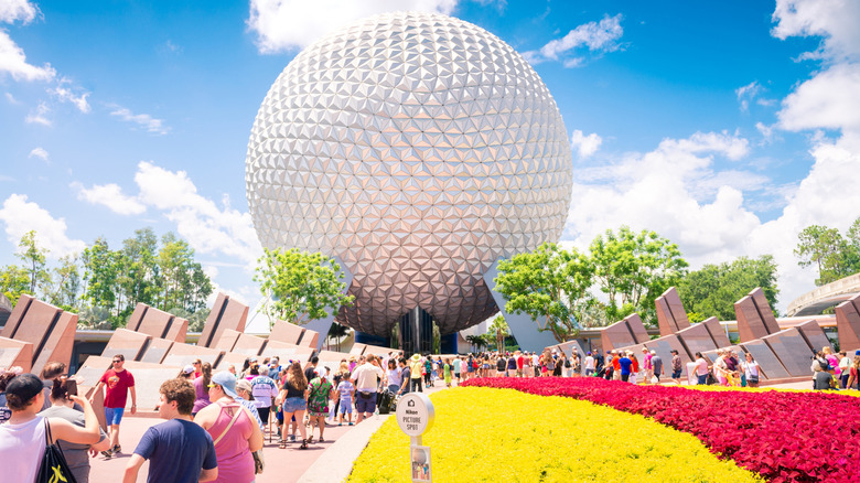 View of crowds milling around and flower beds in front of Spaceship Earth, the iconic sphere entrance at Epcot Park in Walt Disney World Resort, a theme park complex based in Orlando, Florida, USA, pictured on a bright sunny day