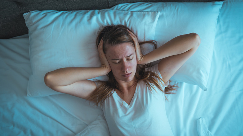 Person on a bed holding their hands on their head in frustration