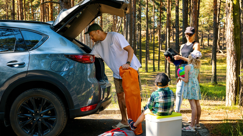 A family unpacks the car at an outdoor camping spot in the woods