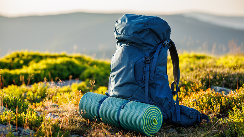 Camping backpack with a rolled yoga mat on the ground