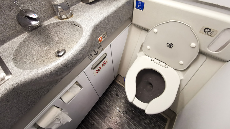 An empty airplane bathroom with the toilet seat up