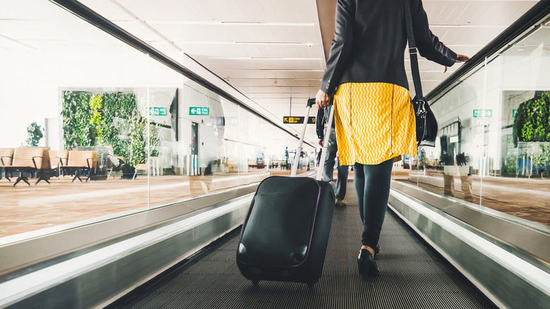 A woman walks through an airport with her suitcase