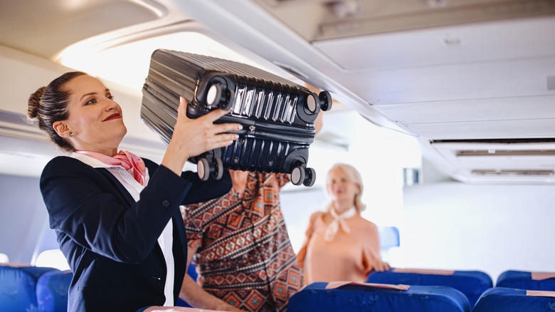Flight attendant stows carry-on suitcase