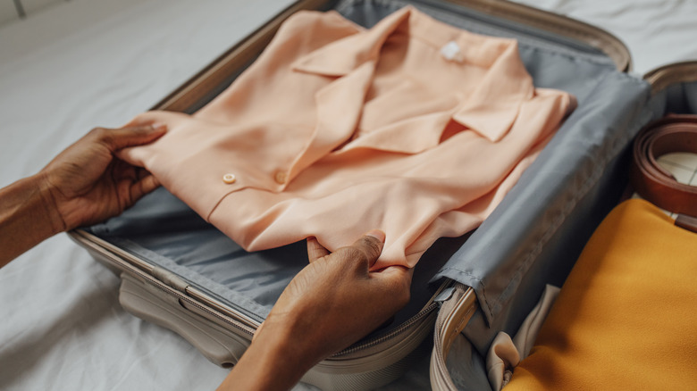 An unidentified woman packs an elegant blouse into her suitcase
