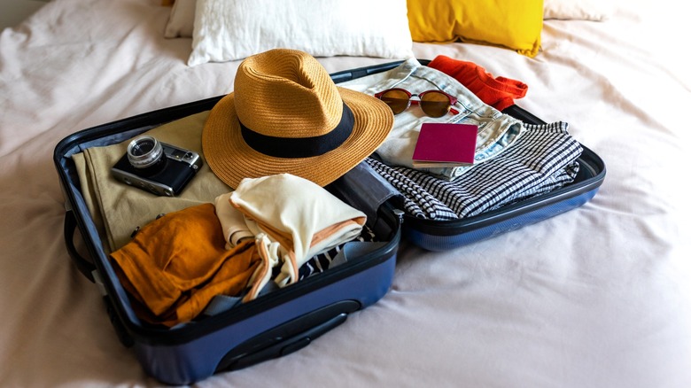 Photo of an open suitcase with hat, sunglasses, and passport on a bed