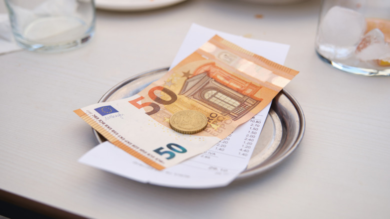 Metal change tray with the bill and a 50 euro note and coins.