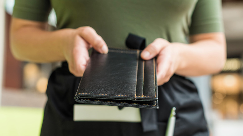 A waitress in an apron holding out a bill folder