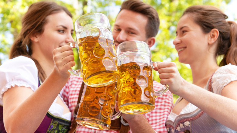 Three people making eye contact while toasting beer steins together