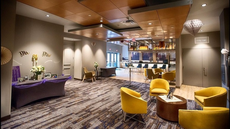 Bar area of the Cambria Hotel, with yellow chairs on a gray and brown carpet in the foreground and the bar in the background