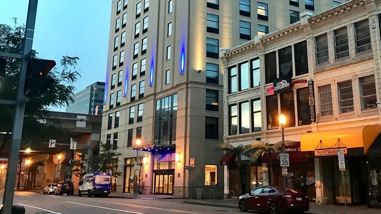 Gray buildings in Pittsburgh's North Shore, one with red and yellow awnings, along a street with a few cars parked out front