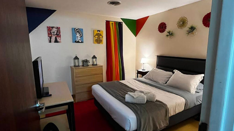 Bedroom with art on the walls and a tan dresser next to a bed with a black headboard and gray and white sheets
