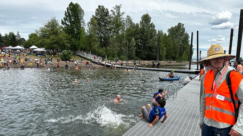A man stands on a swimming dock while people swim and play in the water at Cathedral Park, in Portland, Oregon.