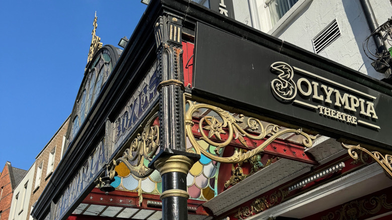 Exterior view of 3Olympia Theatre in Dublin, Ireland on a sunny day with ornate, stained-glass entry awning and black and gold scrollwork