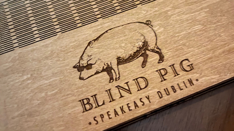 Close-up of etched wooden menu at the Blind Pig Speakeasy Dublin with the bar's pig in sunglasses logo
