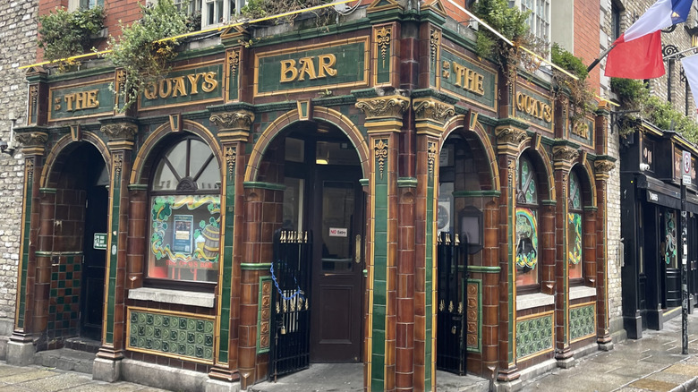 Facade of The Quays Bar, with gold and forest green tile work, in the Temple Bar District, Dublin, Ireland on an overcast day