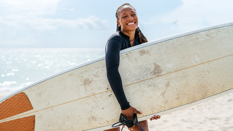 A surfer in a black wetsuit holding a white board on the beach in Miami, on Florida's east coast