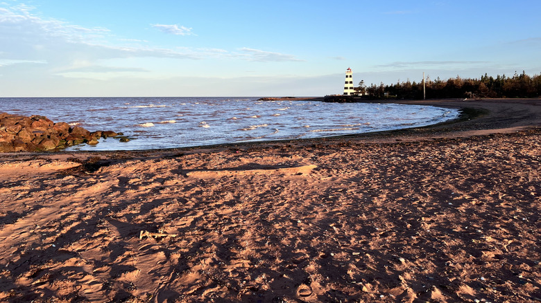 Red sandy beach with lighthouse in background at sunset