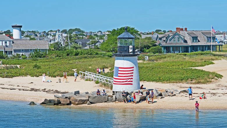Nantucket beachfront with a little lighthouse and people running on the beach