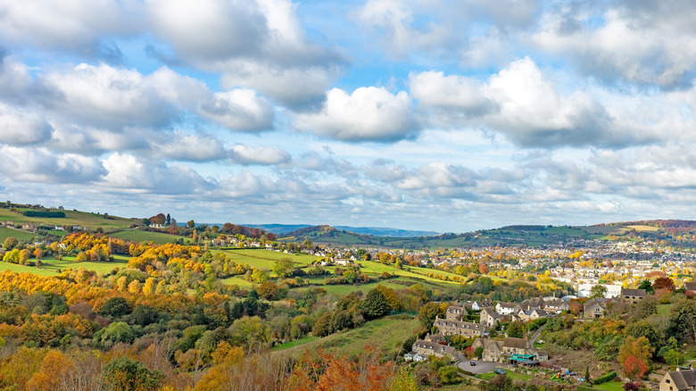 Rolling hills turning golden in fall beneath a cloudy blue sky in Nailsworth Valley in the Cotswolds