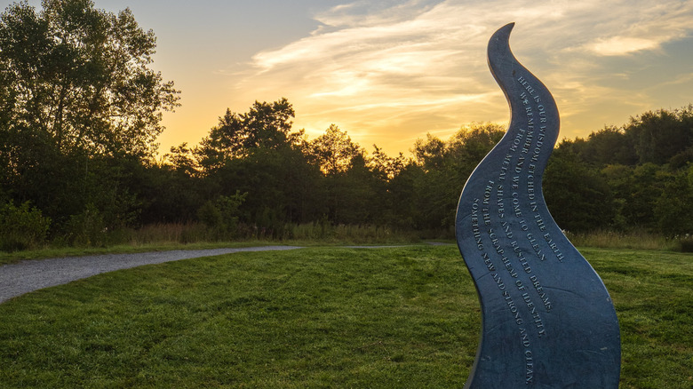 Steel flame sculpture and path at Sutton Manor Woodland in England during sunset