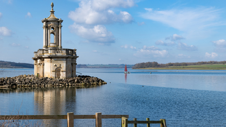 A church on a peninsula in England's Rutland Water with sailboat in distance