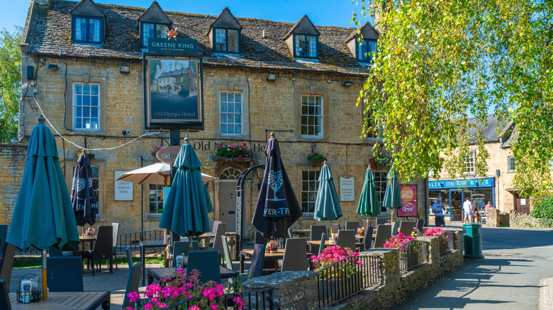Umbrellas and empty tables and chairs outside the honey-colored Old Manse Hotel in Bourton-on-the-Water