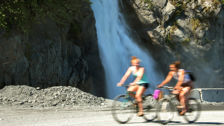 Bicyclists pass a waterfall on the road to Lowell Point from Seward, Alaska