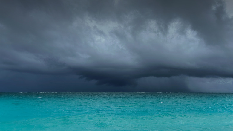 The horizon of the Caribbean Sea shows turbulent waters beneath an overcast sky, filled with dark, dramatic clouds